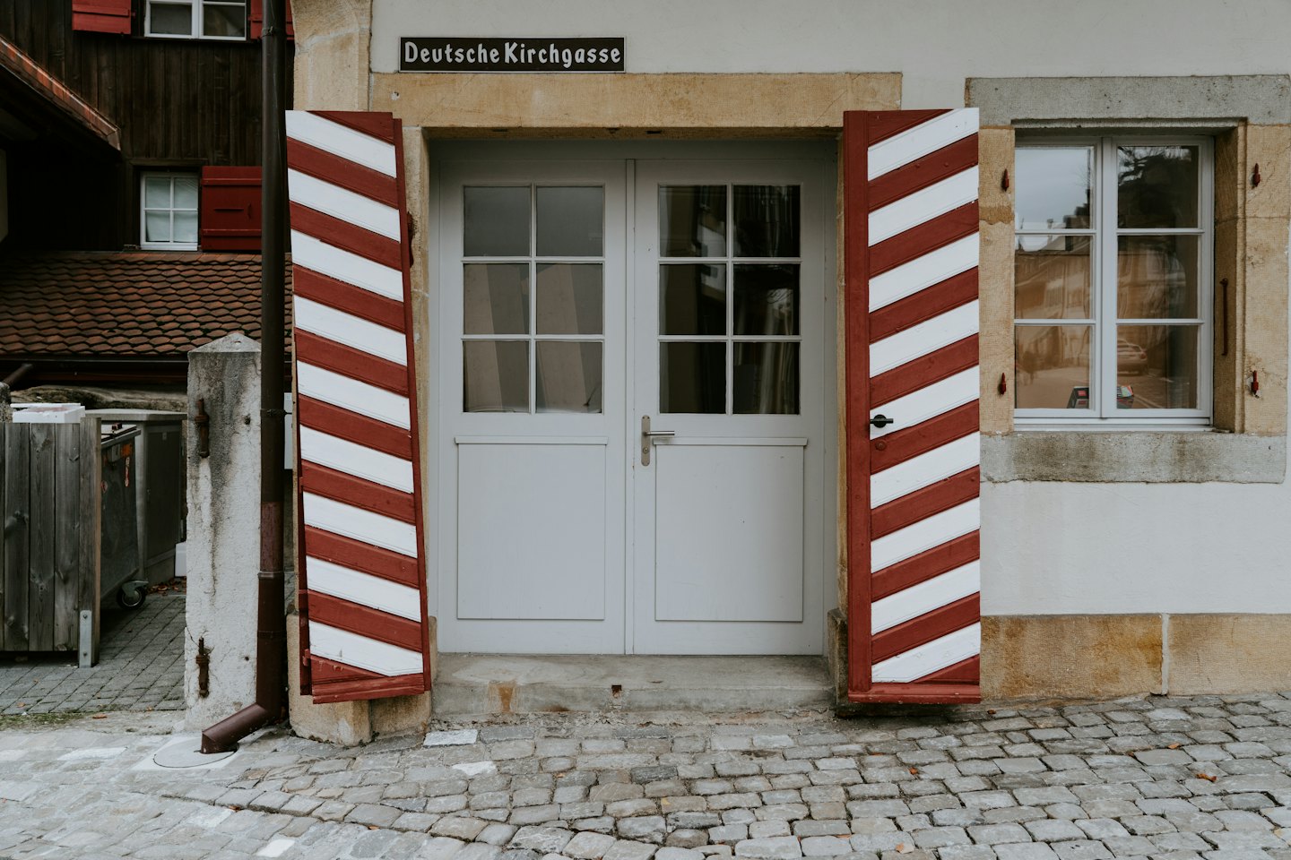 Gebäudeeingang mit grauen Doppeltüren und rot gestreiften Fensterläden.