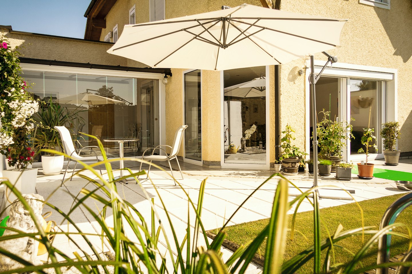 Sonnenschirm spendet Schatten für einen kleinen Tisch vor einem gelben Haus.